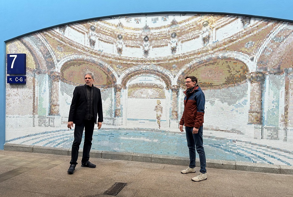Hans Gützlaff (links) und Jochen Wagner stehen vor einem Wandmosaiks auf der Stirnseite der Mittelunterführung des Bahnhofes.
