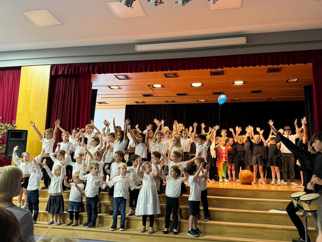Kinder stehen auf einer Bühne und halten die Hände in de Luft. 