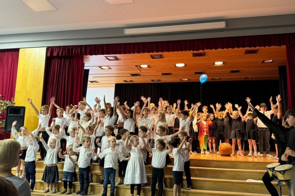 Kinder stehen auf einer Bühne und halten die Hände in de Luft. 